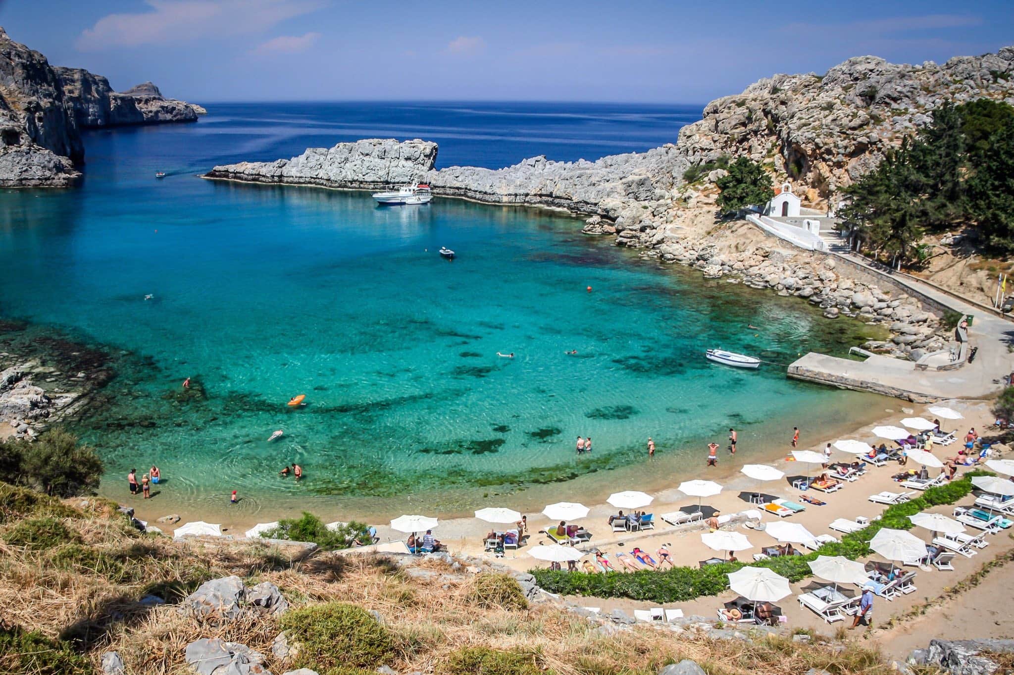 St Paul's Bay near Lindos on Rhodes — a sheltered turquoise cove with a sandy beach, sunbeds and a small white chapel