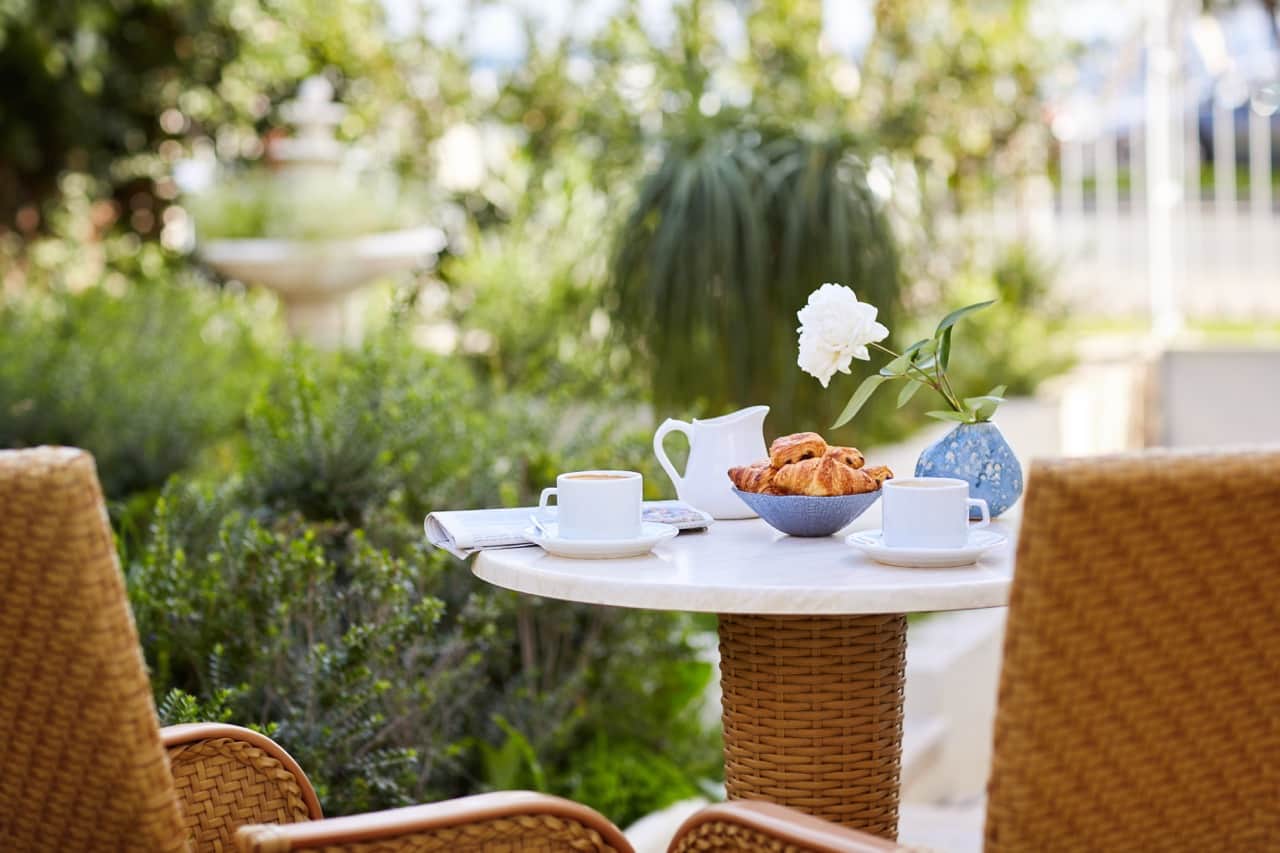 A garden breakfast for two with coffee and croissants on a marble table.