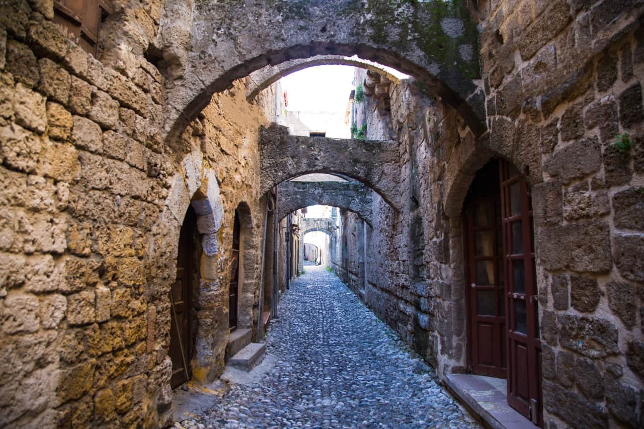 A cobbled lane in Rhodes Old Town framed by a series of weathered stone arches.