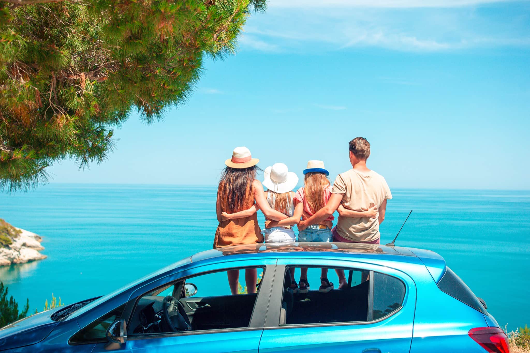 A family standing on a hire car looking out over a turquoise bay on a sunny day — exploring Rhodes by rental car