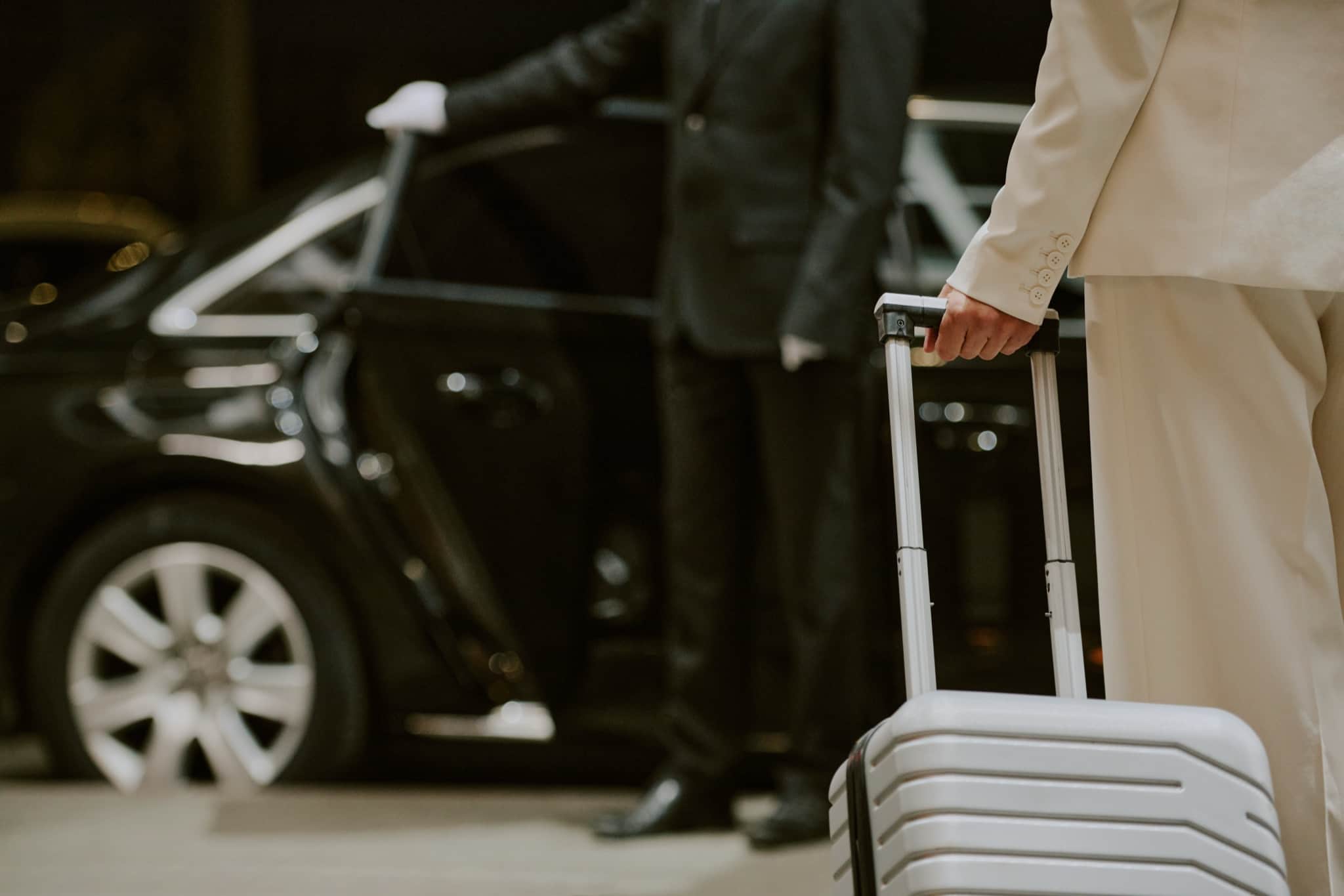 Chauffeur in a dark suit opening a car door for an arriving guest with a suitcase — private Rhodes airport transfer