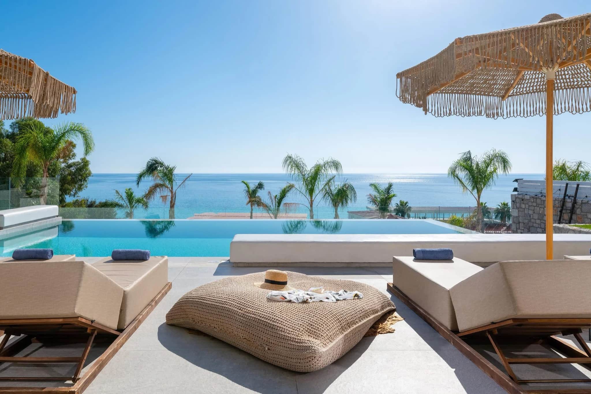 Infinity pool overlooking the sea on a luxury villa terrace with sun loungers, fringed umbrellas and palm trees on Rhodes